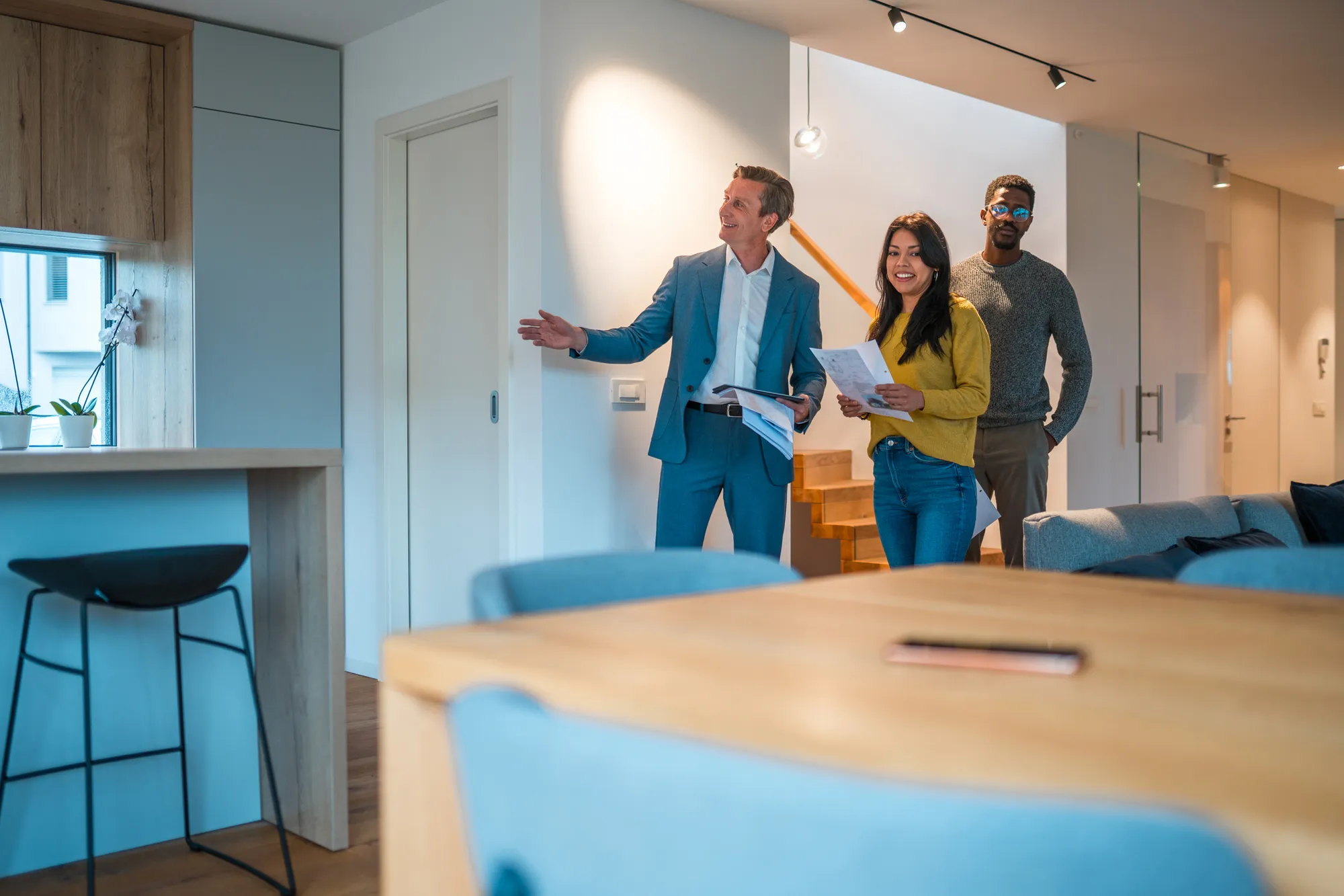 Handsome Caucasian Salesman And Real Estate Agent Showing A Beautiful Apartment To A Young Couple